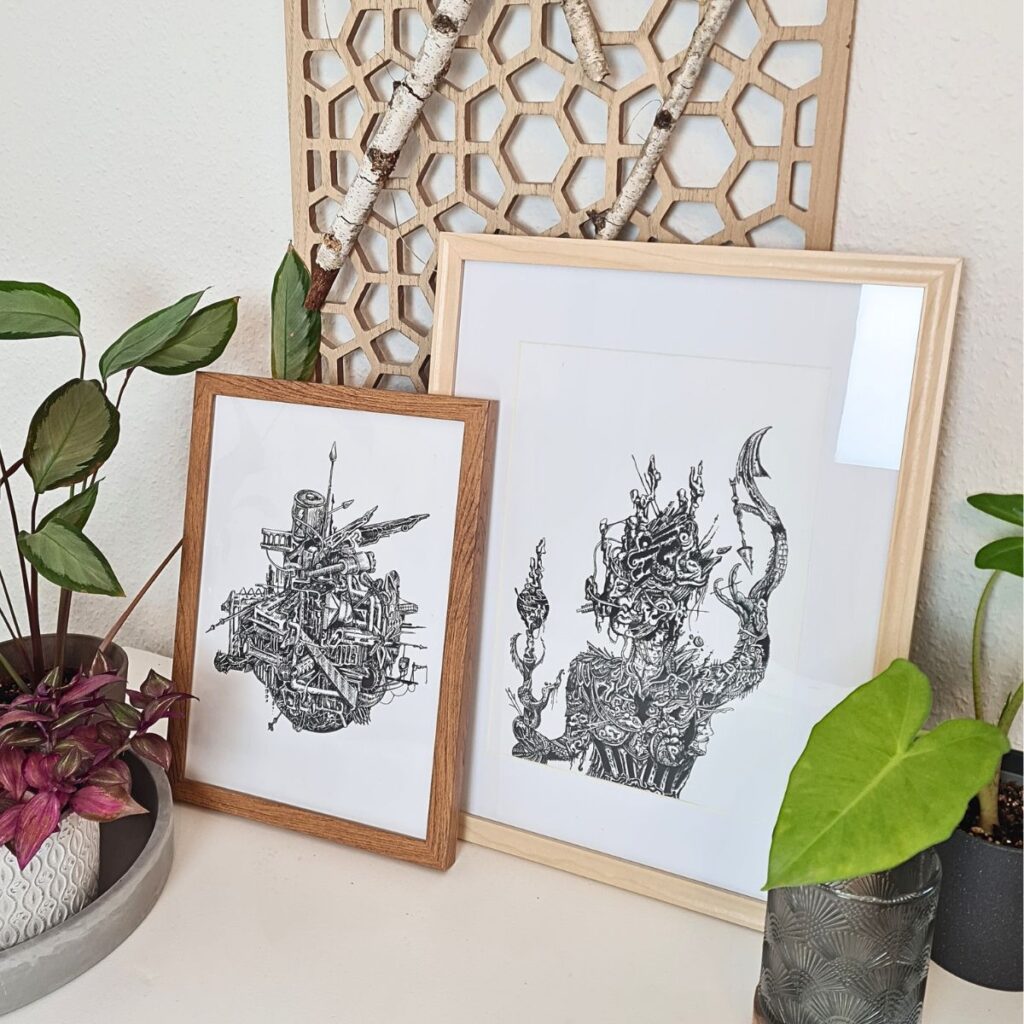 Close-up of two framed art prints with complex black-and-white illustrations, surrounded by plants and geometric wooden decor, highlighting modern and eclectic interior design.