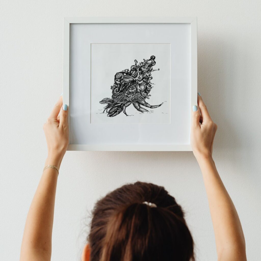 Person holding the "coming home" poster in a white frame against a light wall, showcasing a detailed design of a hermit crab, perfect for adding summer and holiday vibes to home decor.